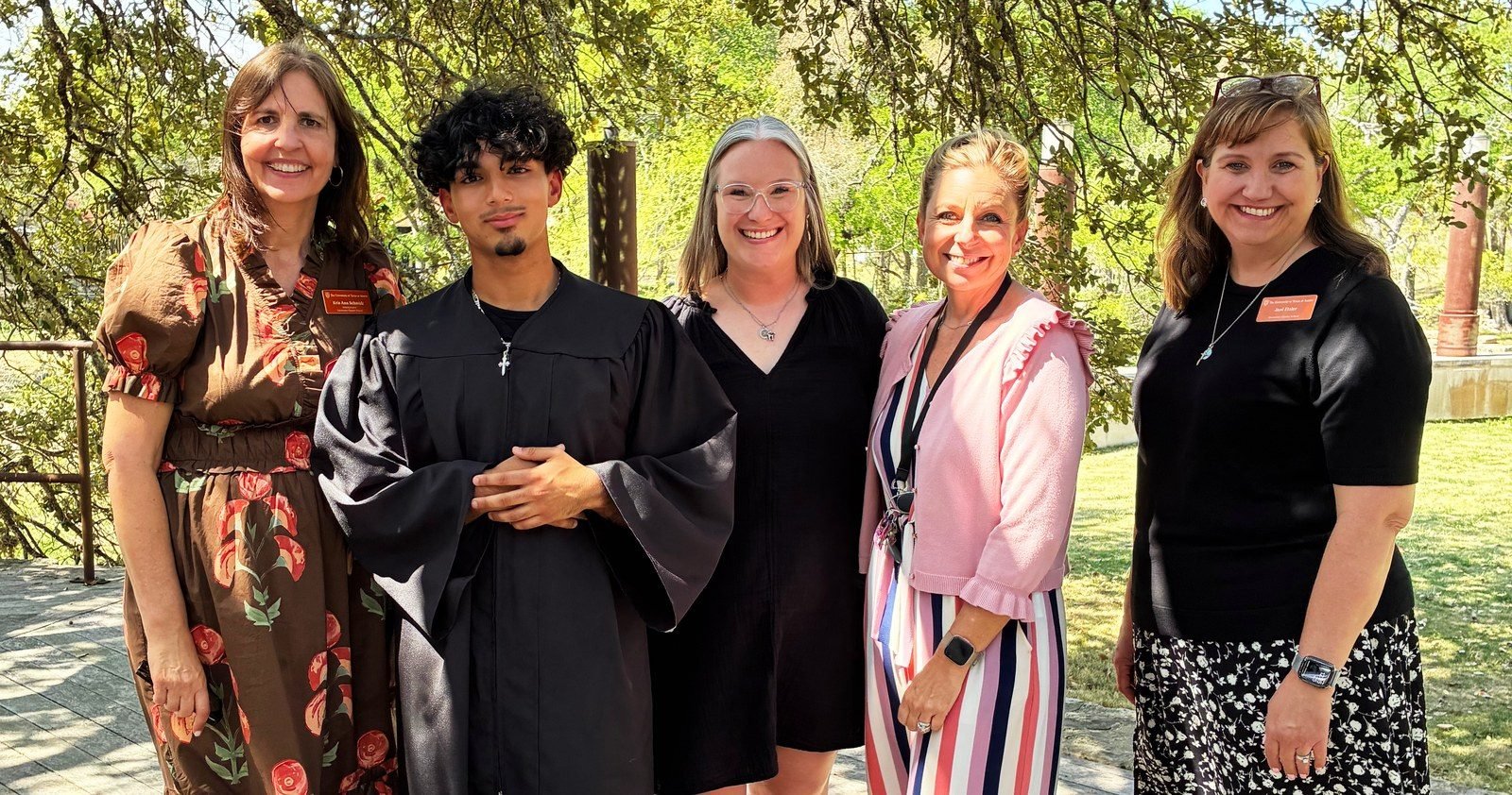 Four UT Charter School staff members standing outdoors with a graduate in a black gown
