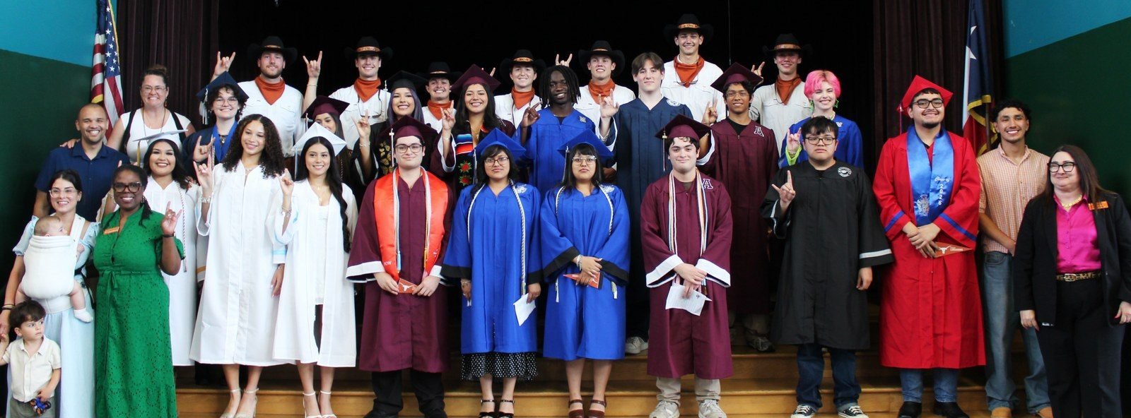 Graduates in caps and gowns gathered with family members and staff on a stage with U.S. and Texas flags